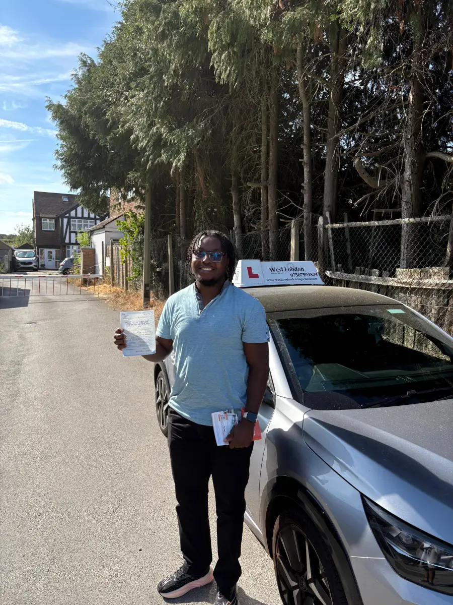 A West London Driving School student holding his practical test pass certificate beside the school car